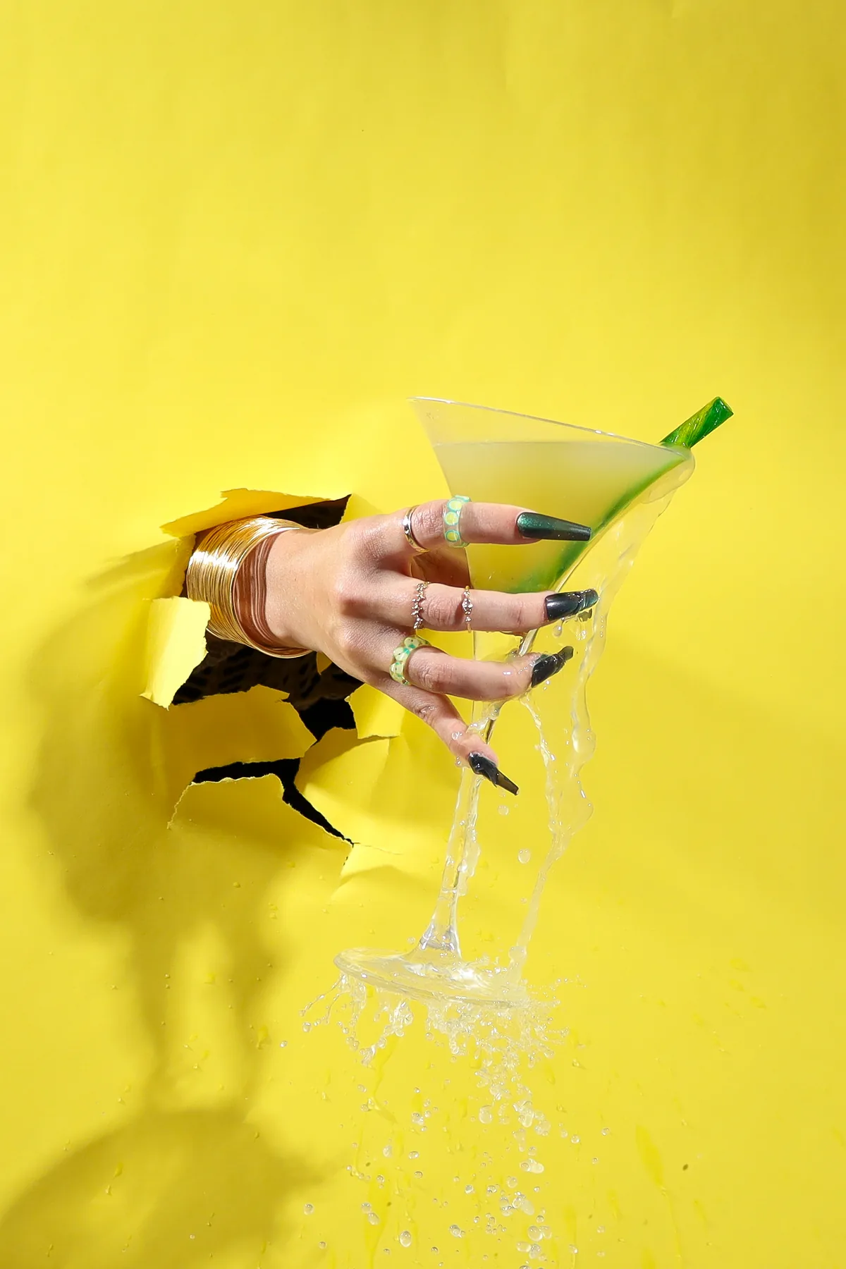 A green cocktail reaching through a bright yellow backdrop