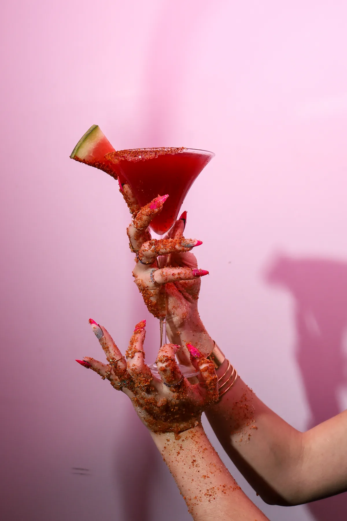 A red cocktail held against a pink backdrop